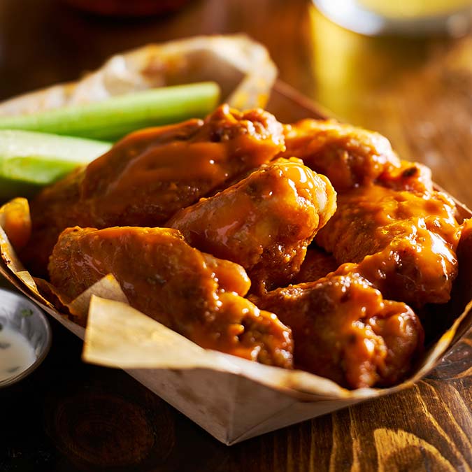 Spicy buffalo chicken wings from E.J.'s Diner Wausau with celery sticks on a wooden table.