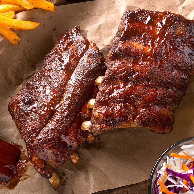 Barbecued ribs with sauce, fries, and coleslaw at E.J.'s Diner Wausau on brown parchment paper.
