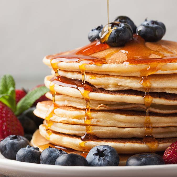 Stack of pancakes at E.J.'s Diner Wausau, topped with blueberries, syrup, and assorted berries.