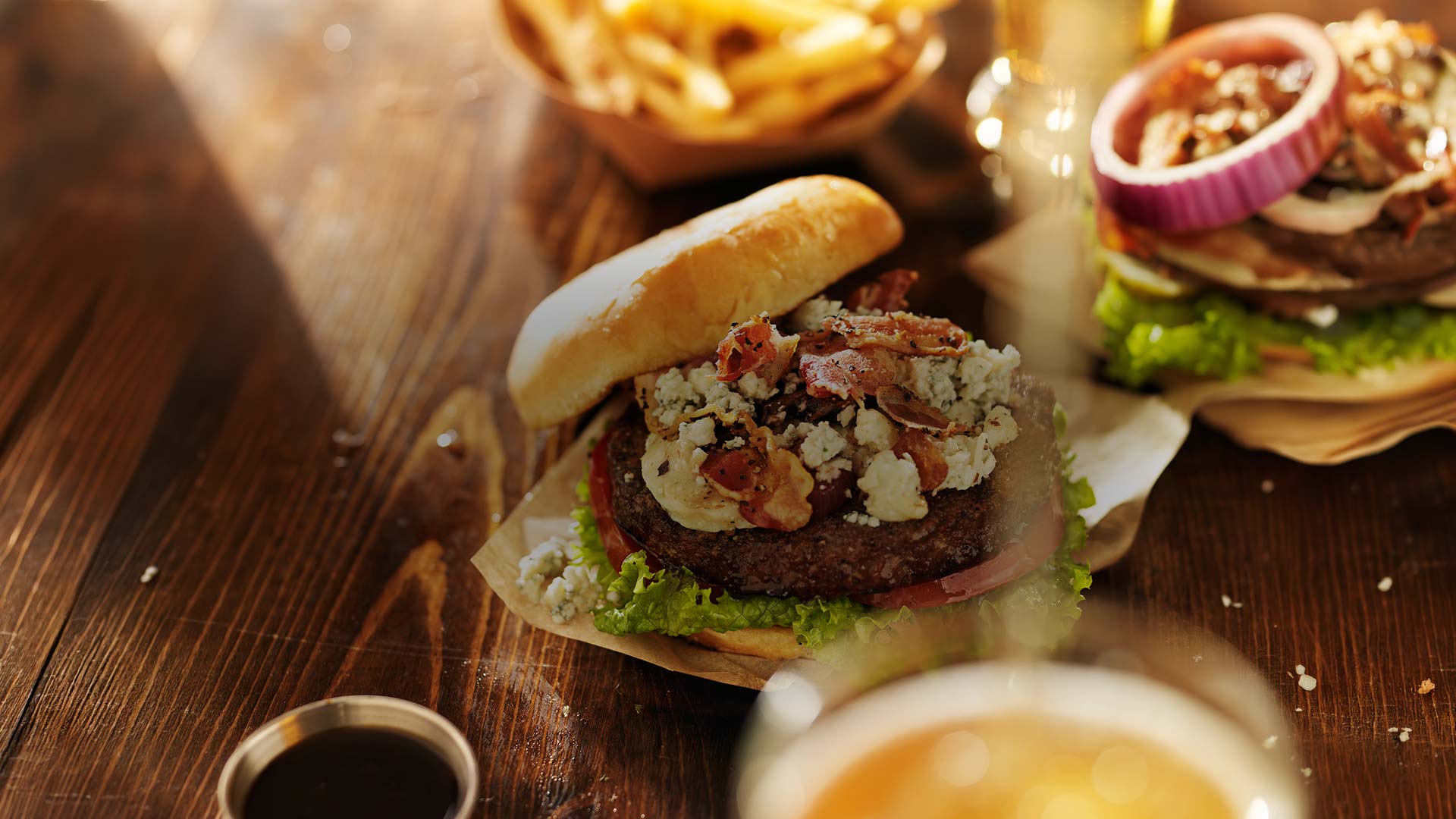 Gourmet burger with lettuce, tomato, blue cheese, and bacon on a wooden table next to fries served at E.J.'s Diner in Wausau, WI.