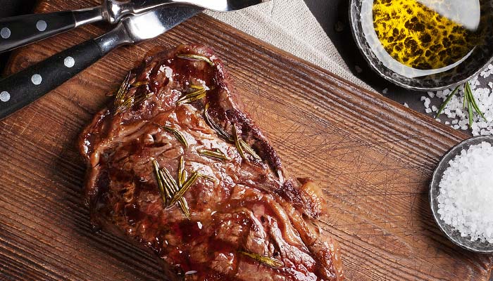Grilled steak with rosemary, perfect for lunch in Wausau WI, on a board with salt and oil.