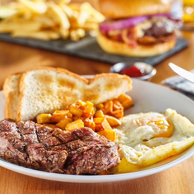 Steak, eggs, toast, and potatoes at E.J.'s Diner Wausau, with fries and a burger behind.